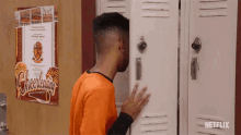 a man standing in front of a locker with a cheerleading poster on the wall behind him
