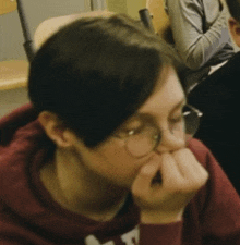 a person wearing glasses and a red sweatshirt with the letter t on it