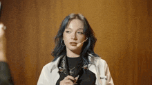 a woman with blue hair is wearing a microphone and a white jacket that says s.a.u.t. all on it