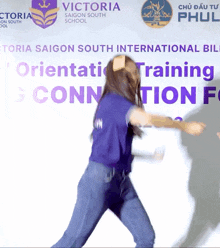 a woman in a purple shirt is dancing in front of a victoria saigon south international school banner