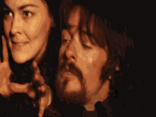 a man and a woman are standing next to each other in a dark room . the man has a beard .