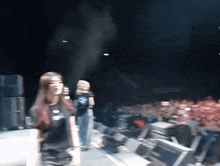 a woman in a black t-shirt with the letter s on it stands on a stage in front of a crowd