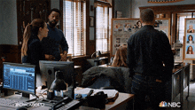 a group of people standing in a room with a nbc logo on the bottom