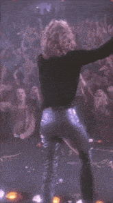 a woman in leather pants is dancing in front of a crowd of people