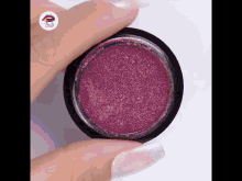 a woman 's hand is holding a container of purple powder