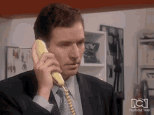 a man in a suit is talking on a yellow phone with nuestra tele written on the bottom right