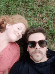 a man and a woman laying in the grass with sunglasses on