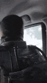 a man with a backpack is sitting in the back seat of a car looking out the window