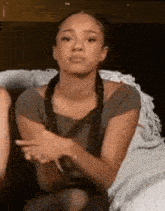 a woman is sitting on a bed with her arms crossed and making a face .