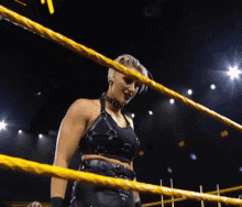 a woman is standing in a wrestling ring with a yellow rope