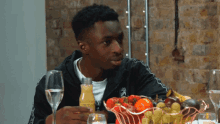 a young man sits at a table with a bowl of fruit and a bottle of juice