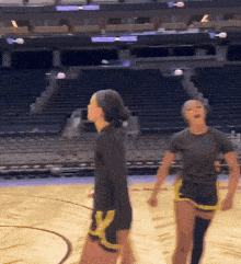 two women playing basketball on a court with empty seats in the background