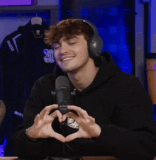 a man wearing headphones is making a heart shape with his hands in front of a microphone