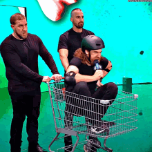 a man wearing a helmet is sitting in a shopping cart being pushed by two other men