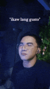 a man wearing glasses and ear buds says " ikaw lang gusto " in front of a christmas tree .