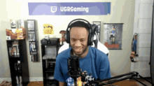 a man wearing headphones stands in front of a sign that says ugrgaming