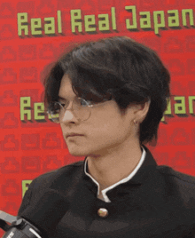 a man wearing glasses stands in front of a sign that says " real real japan "