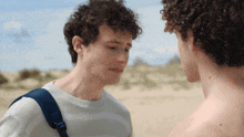 a man with a backpack looks down at another man with curly hair