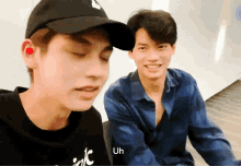 two young men are sitting next to each other and one of them is wearing a hat that says uh