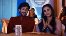 a man and a woman are sitting at a table with bottles of water .