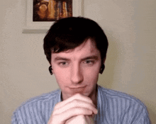 a man wearing ear buds and a striped shirt has his hands folded in front of his face