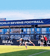 a soccer player is doing a handstand in front of a sign that says world sevens football
