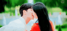 a man and woman are kissing in front of a fountain in a park .