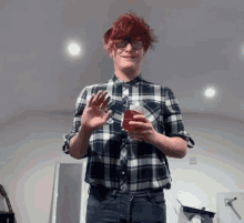 a man in a plaid shirt holds a glass of red liquid in his hand
