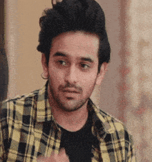a young man wearing a plaid shirt and a black shirt is looking at the camera .