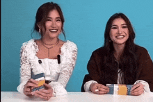 two women are sitting at a table with a blue background