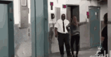 a man and a woman are walking down a hallway with a crown on the bottom right corner