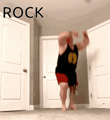 a man in a black tank top and red shorts is dancing in a room with the word rock written above him