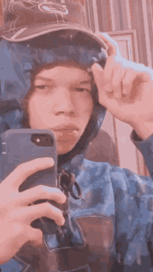 a young man is taking a selfie with his phone while wearing a hat and a hoodie .