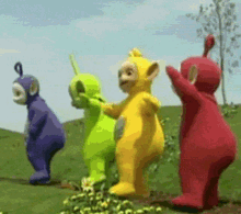 a group of teletubbies standing in a grassy field