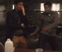two men are dancing in a kitchen with a milk carton in the background .