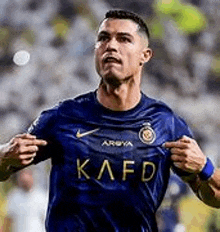 a soccer player wearing a blue shirt with the word kafd on it is running on a field .