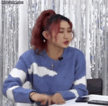 a woman with red hair and a blue and white sweater is sitting at a table .