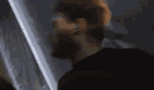 a man with a beard is standing in a dark room with a light shining on his face .
