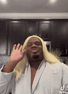 a man wearing a blonde wig and a white robe is making a funny face .
