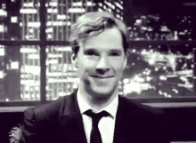 a man in a suit and tie is smiling in front of a window in a black and white photo .