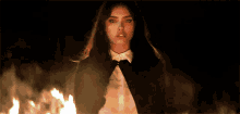 a woman in a tuxedo and white shirt is standing in front of a fire