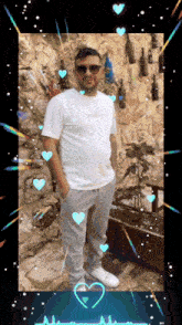 a man wearing sunglasses and a white shirt stands in front of a stone wall with bottles hanging on it