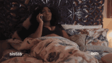 a woman laying in bed talking on a cell phone with the sistas logo visible