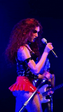 a woman is singing into a microphone while playing a guitar