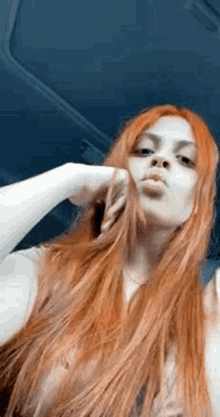 a woman with long red hair is taking a selfie in a car with her hand in her hair .