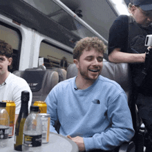 a man wearing a blue north face sweatshirt laughs while sitting on a train