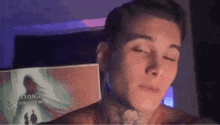 a man with a tattoo on his neck is sitting in front of a computer screen with his eyes closed .