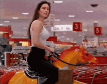 a woman in a white tank top is riding a mechanical horse in a store