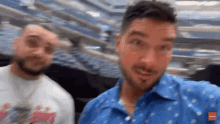 two men are standing next to each other in a stadium and one is wearing a blue shirt