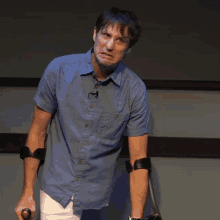 a man in a blue shirt is holding a crutch and making a face